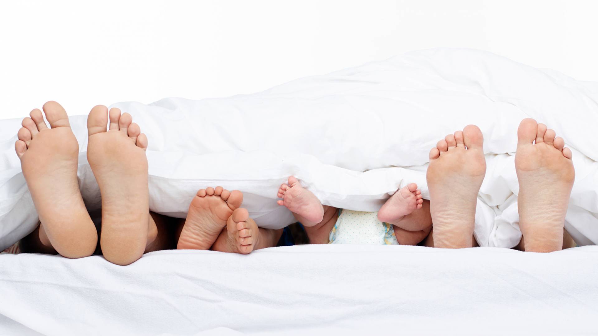 Füße von Eltern und Babys scheinen unter einer Decke hervor