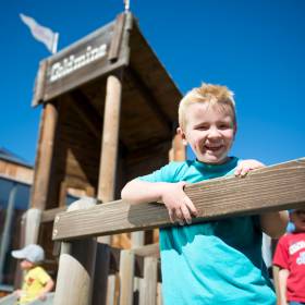 Junge schaut von Klettergerüst auf dem Spielplatz zur Kamera