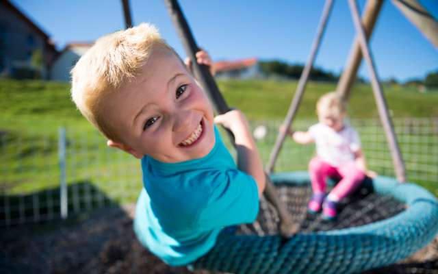 Zwei Kinder schaukeln auf dem Spielplatz im Familienhotel Schreinerhof