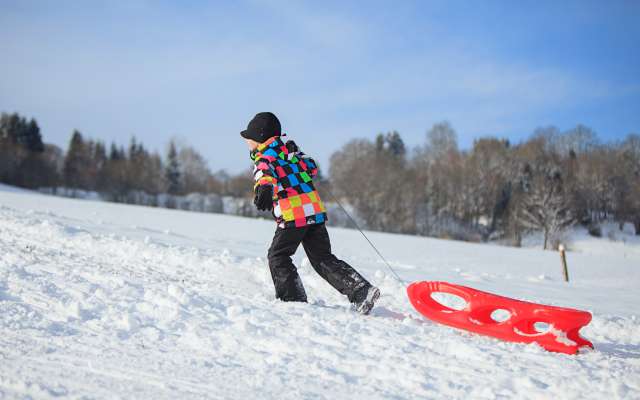 Kind mit Rodel auf einem verschneiten Hügel im bayerischen Wald