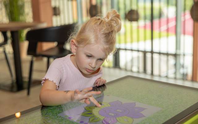 Kleinkind sitzt am digitalen Spieltisch im Babyhotel Deutschland