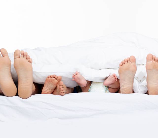 Elternfüße und Babyfüße strecken aus Bett heraus