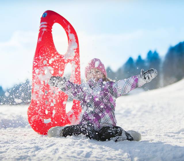 Kind spielt mit Rodel im Schnee