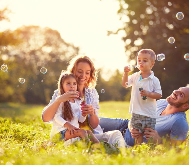 Familie sitzt im Grünen und macht Seifenblasen