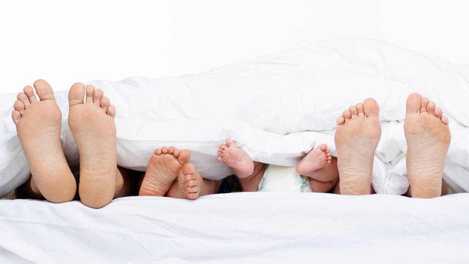 Elternfüße und Babyfüße strecken aus Bett heraus