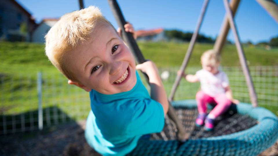 Kinder schaukeln auf Spielplatz im Familienhotel Schreinerhof