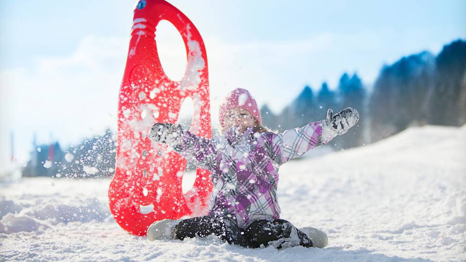 Kind mit Rodel spielt im Schnee im bayerischen Wald